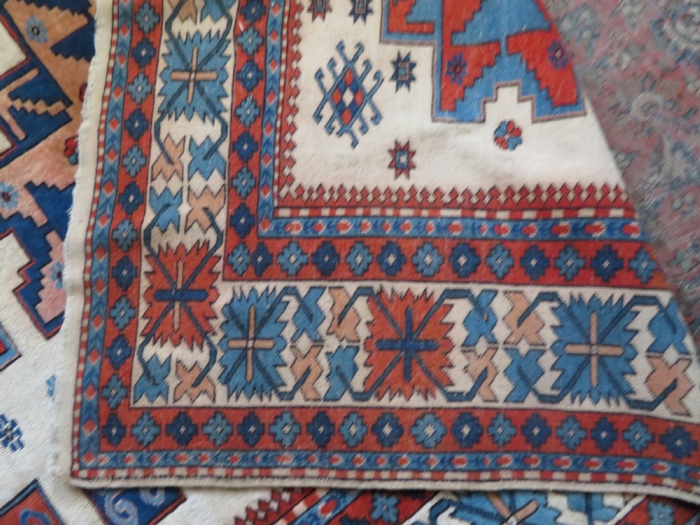 A hand-knotted wool carpet featuring three large geometric medallions in red, blue, and terracotta on a cream field, framed by multi-layered geometric borders. View XV