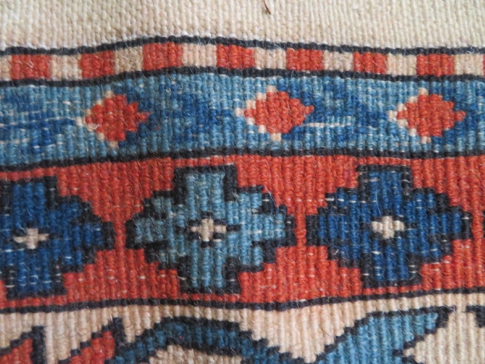 A hand-knotted wool carpet featuring three large geometric medallions in red, blue, and terracotta on a cream field, framed by multi-layered geometric borders. View XVI