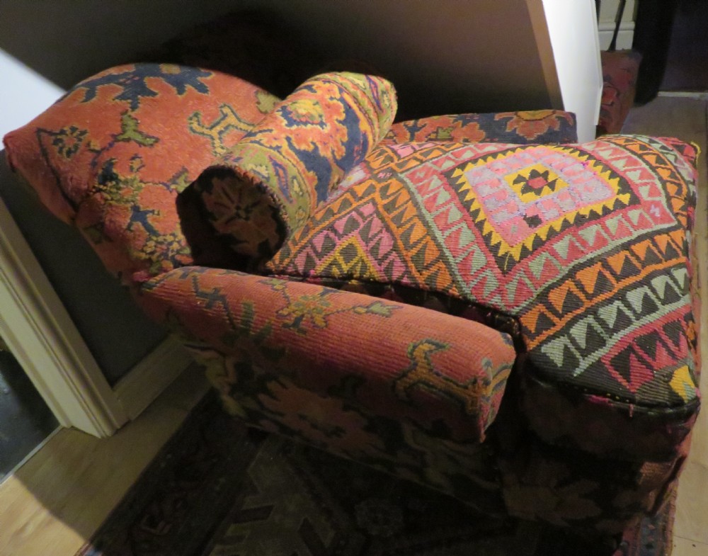 A low-slung, deep-seated Howard and Sons club armchair upholstered in a terracotta red and multi-coloured Ushak carpet pattern with turned legs on brass castors. View XXII