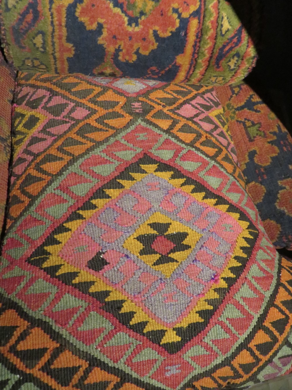 A low-slung, deep-seated Howard and Sons club armchair upholstered in a terracotta red and multi-coloured Ushak carpet pattern with turned legs on brass castors. View XXIV