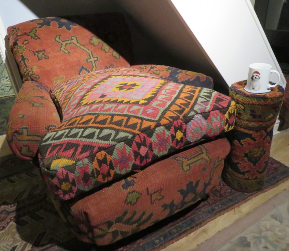 A low-slung, deep-seated Howard and Sons club armchair upholstered in a terracotta red and multi-coloured Ushak carpet pattern with turned legs on brass castors. View XXV