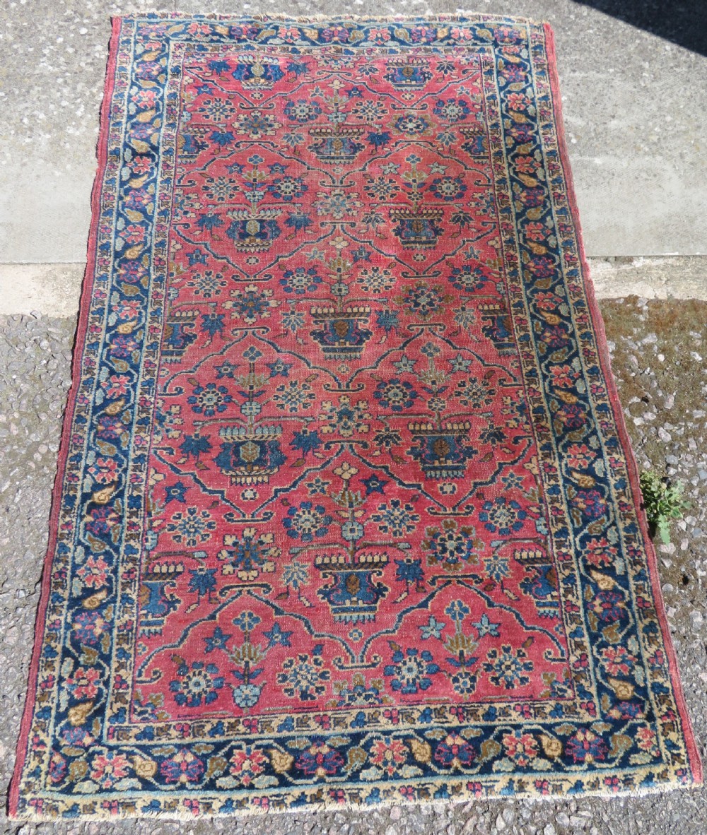 An antique West Persian Sarouk hand-knotted wool rug featuring a rose pink field adorned with floral vase motifs and a navy blue floral border.