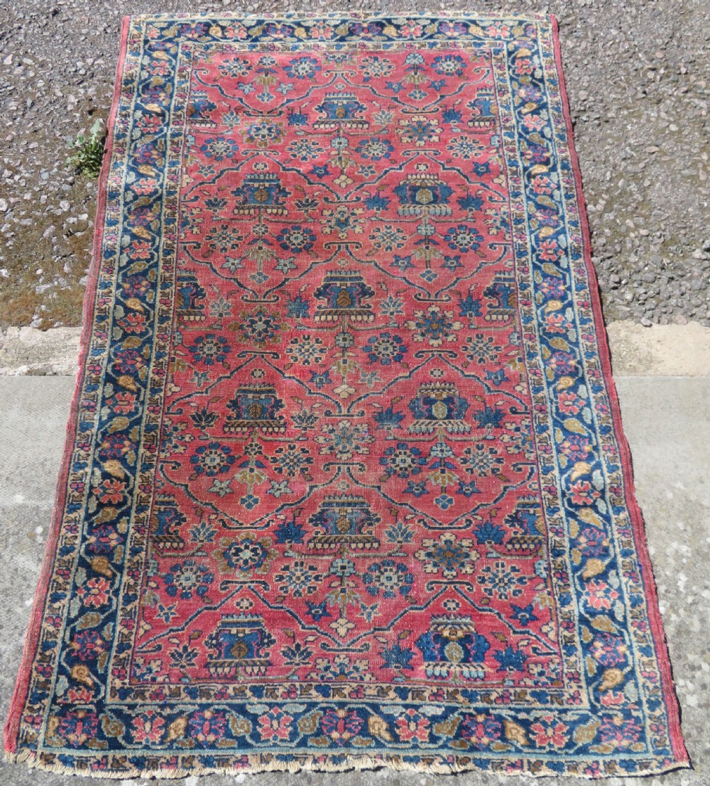 An antique West Persian Sarouk hand-knotted wool rug featuring a rose pink field adorned with floral vase motifs and a navy blue floral border. View II