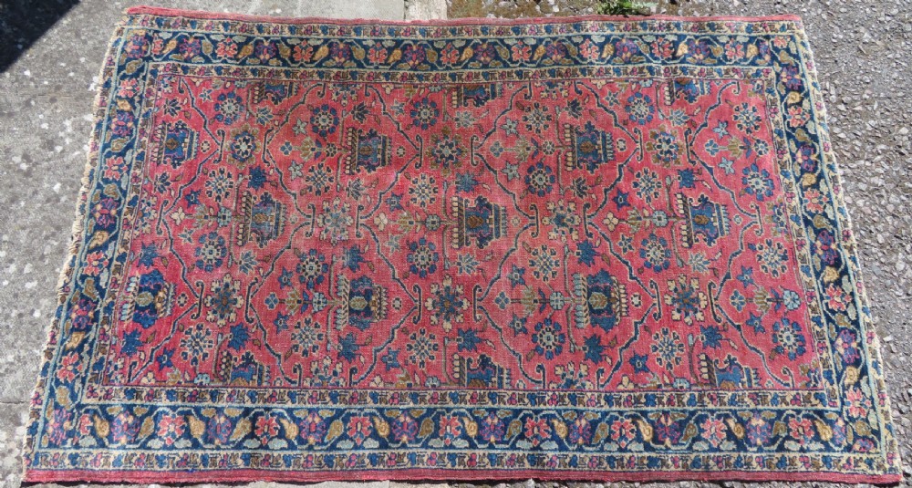 An antique West Persian Sarouk hand-knotted wool rug featuring a rose pink field adorned with floral vase motifs and a navy blue floral border. View IV