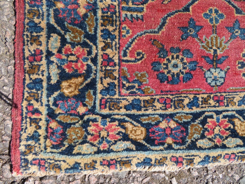 An antique West Persian Sarouk hand-knotted wool rug featuring a rose pink field adorned with floral vase motifs and a navy blue floral border. View VII