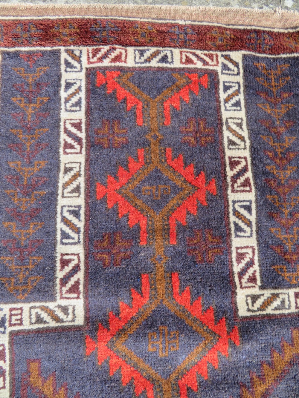 A hand-knotted antique Persian Baluch prayer rug with geometric diamond motifs in rust red and brown against a dark blue central field. View III