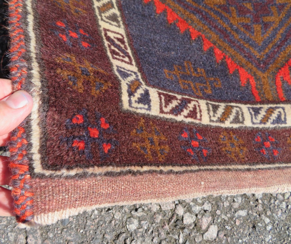 A hand-knotted antique Persian Baluch prayer rug with geometric diamond motifs in rust red and brown against a dark blue central field. View IV