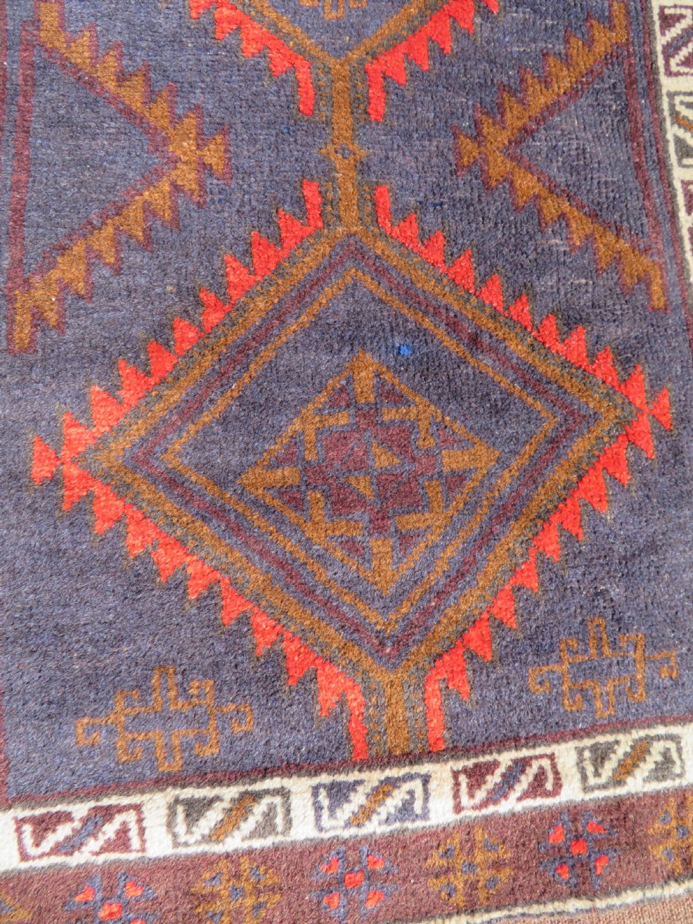 A hand-knotted antique Persian Baluch prayer rug with geometric diamond motifs in rust red and brown against a dark blue central field. View V
