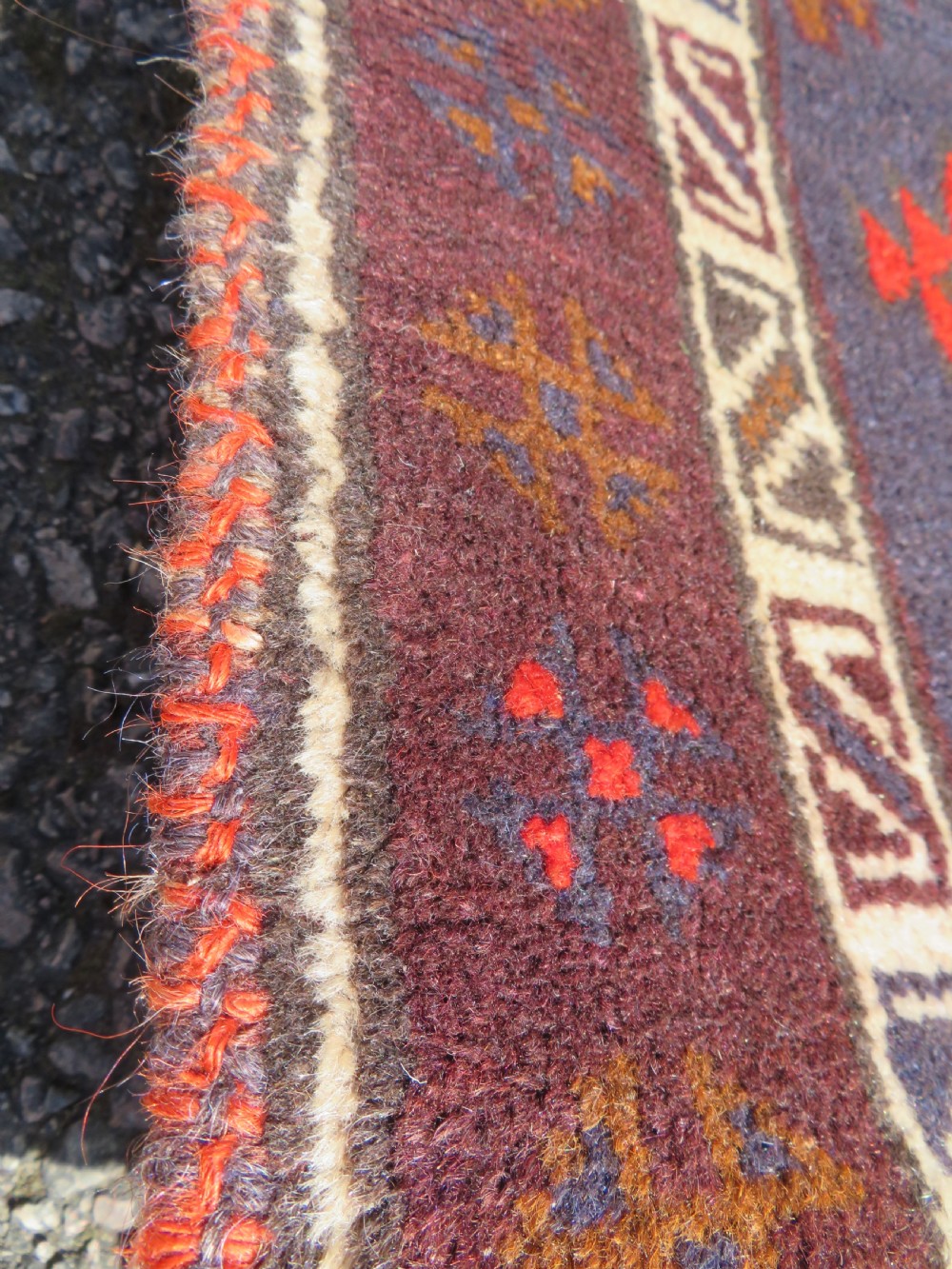A hand-knotted antique Persian Baluch prayer rug with geometric diamond motifs in rust red and brown against a dark blue central field. View VI
