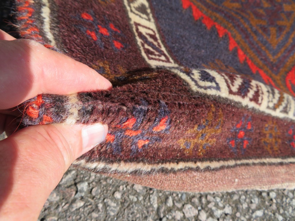A hand-knotted antique Persian Baluch prayer rug with geometric diamond motifs in rust red and brown against a dark blue central field. View VII
