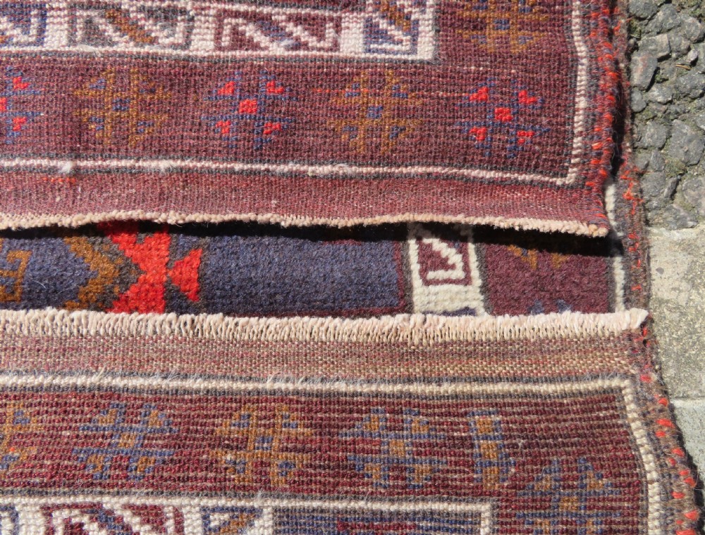A hand-knotted antique Persian Baluch prayer rug with geometric diamond motifs in rust red and brown against a dark blue central field. View IX