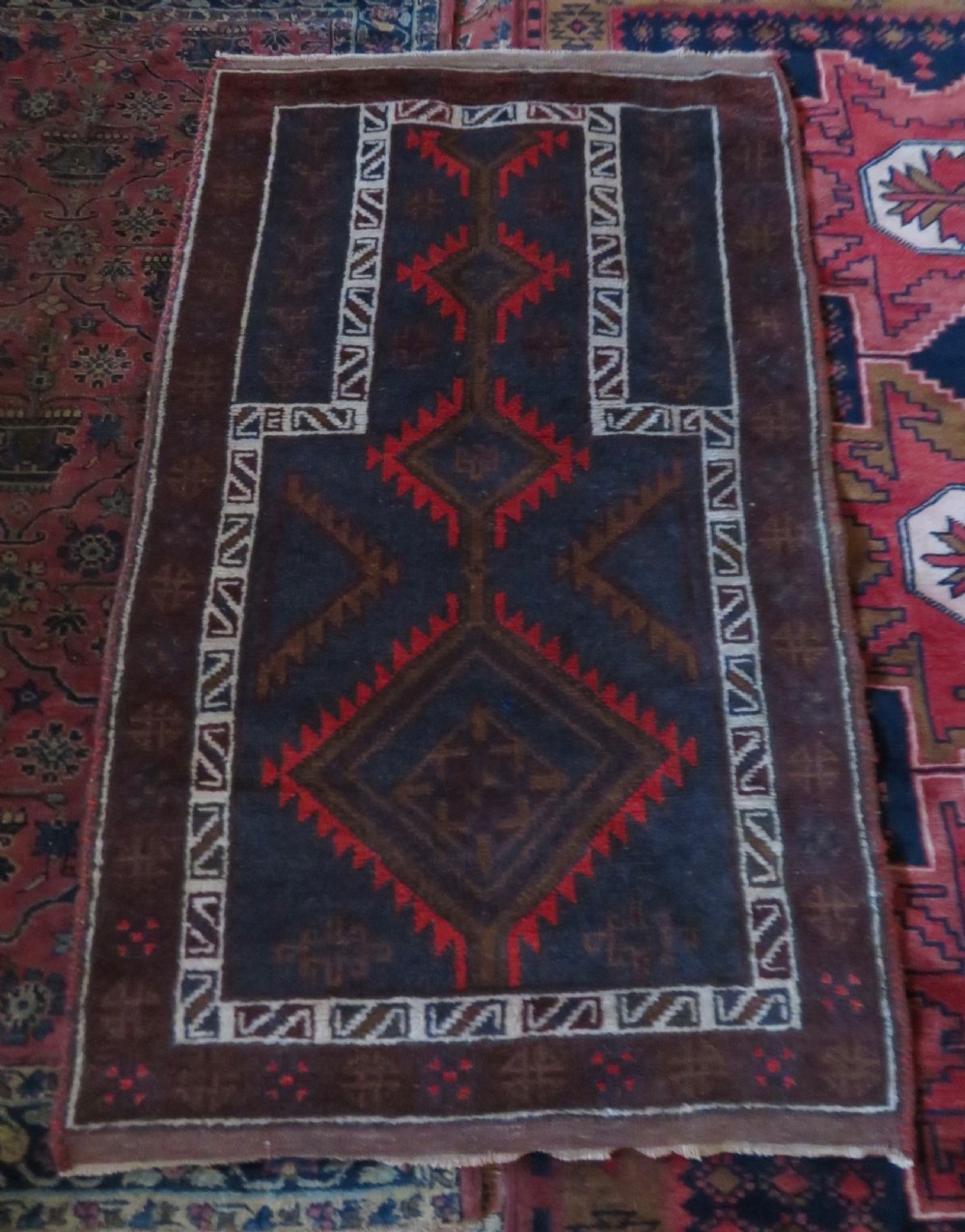 A hand-knotted antique Persian Baluch prayer rug with geometric diamond motifs in rust red and brown against a dark blue central field. View XI