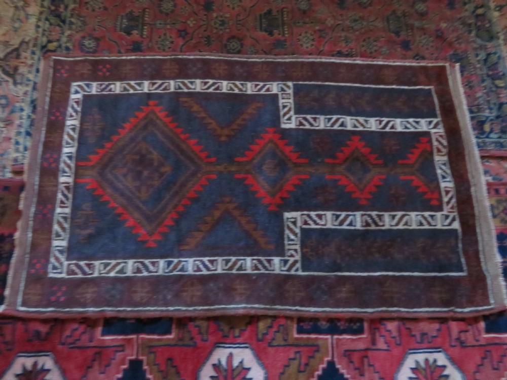 A hand-knotted antique Persian Baluch prayer rug with geometric diamond motifs in rust red and brown against a dark blue central field. View XII