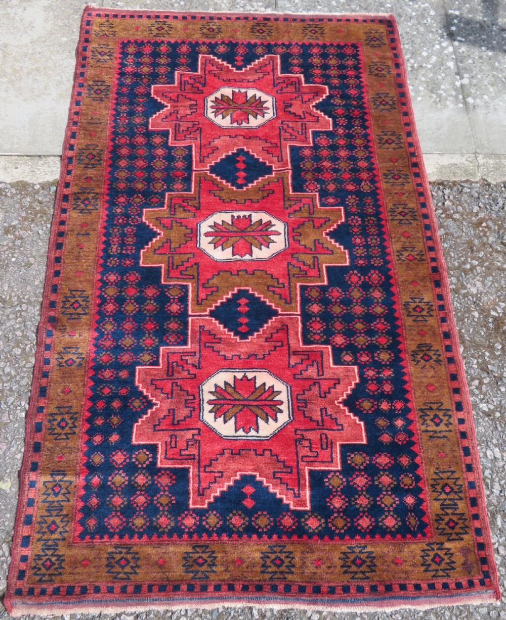 A handwoven Turkish wool rug featuring three central red star medallions on a dark navy blue field with geometric borders in ochre brown.