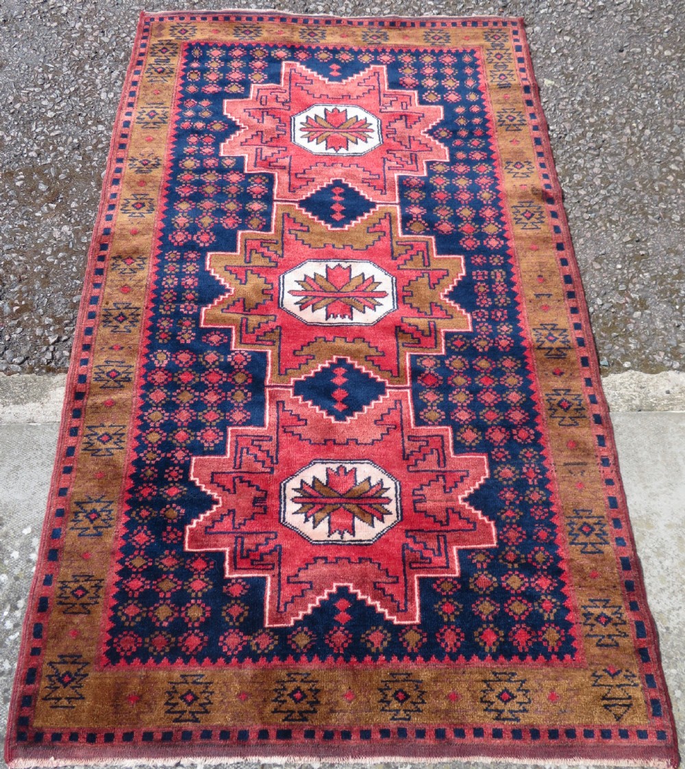 A handwoven Turkish wool rug featuring three central red star medallions on a dark navy blue field with geometric borders in ochre brown. View II