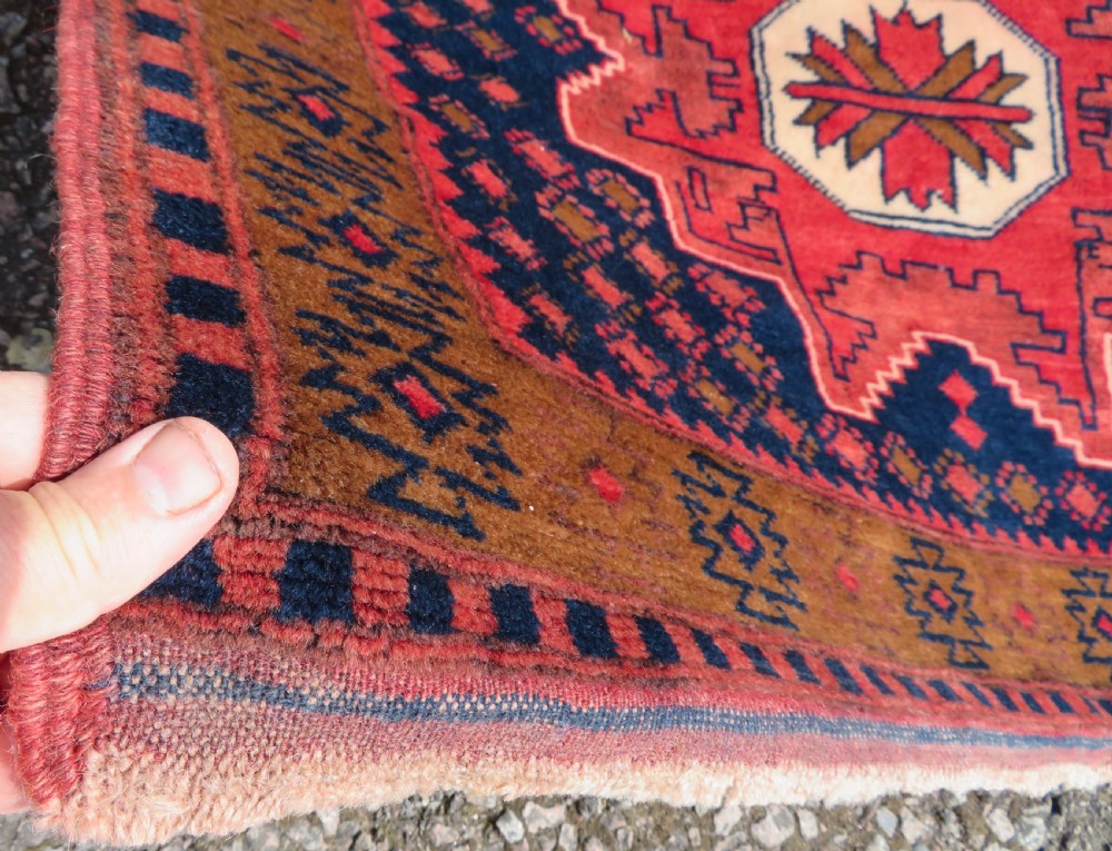 A handwoven Turkish wool rug featuring three central red star medallions on a dark navy blue field with geometric borders in ochre brown. View IV