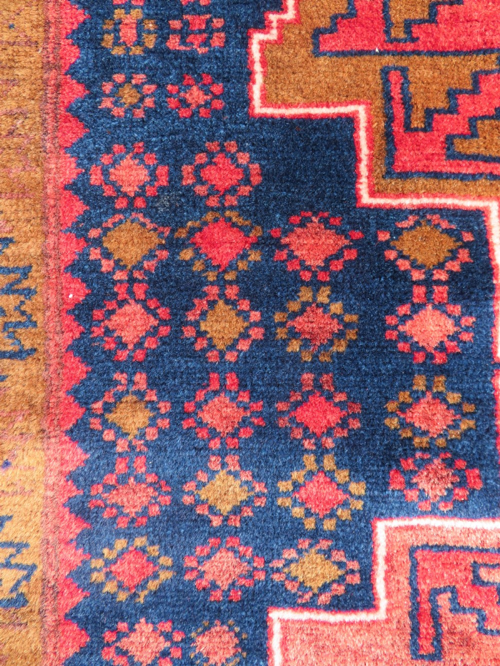 A handwoven Turkish wool rug featuring three central red star medallions on a dark navy blue field with geometric borders in ochre brown. View V