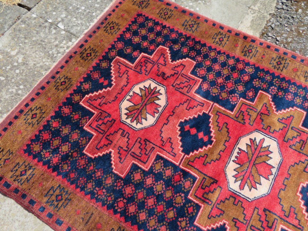 A handwoven Turkish wool rug featuring three central red star medallions on a dark navy blue field with geometric borders in ochre brown. View VII