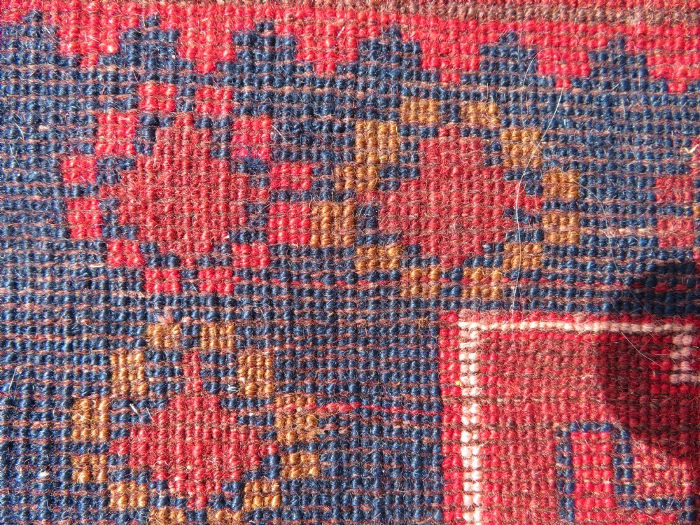 A handwoven Turkish wool rug featuring three central red star medallions on a dark navy blue field with geometric borders in ochre brown. View XI