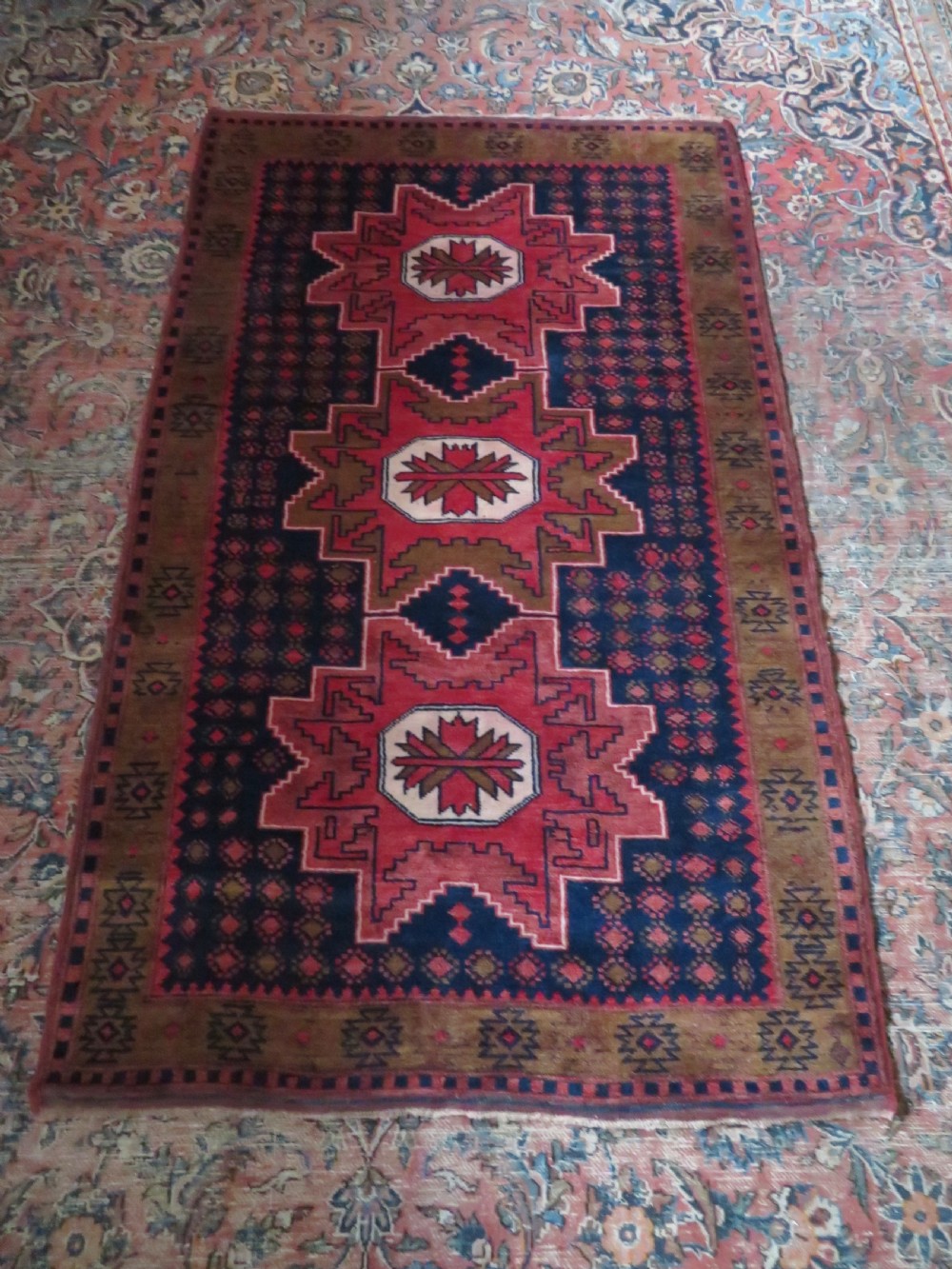 A handwoven Turkish wool rug featuring three central red star medallions on a dark navy blue field with geometric borders in ochre brown. View XII