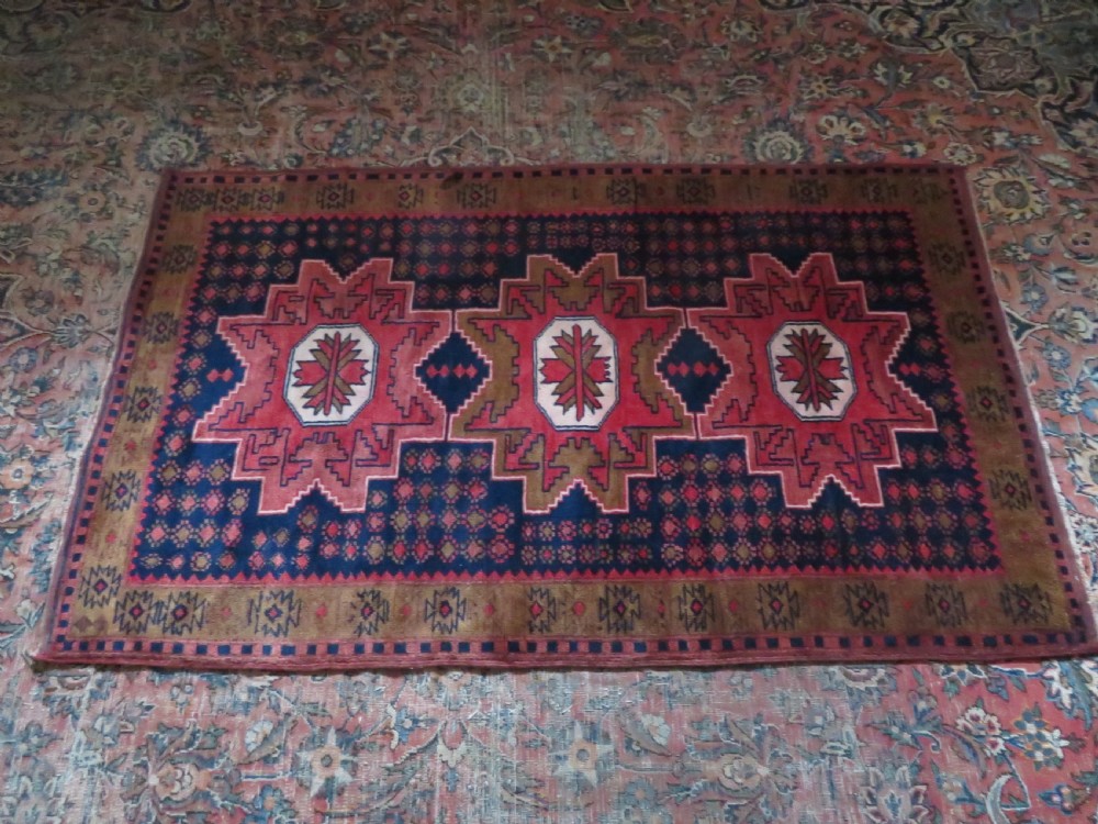 A handwoven Turkish wool rug featuring three central red star medallions on a dark navy blue field with geometric borders in ochre brown. View XIII