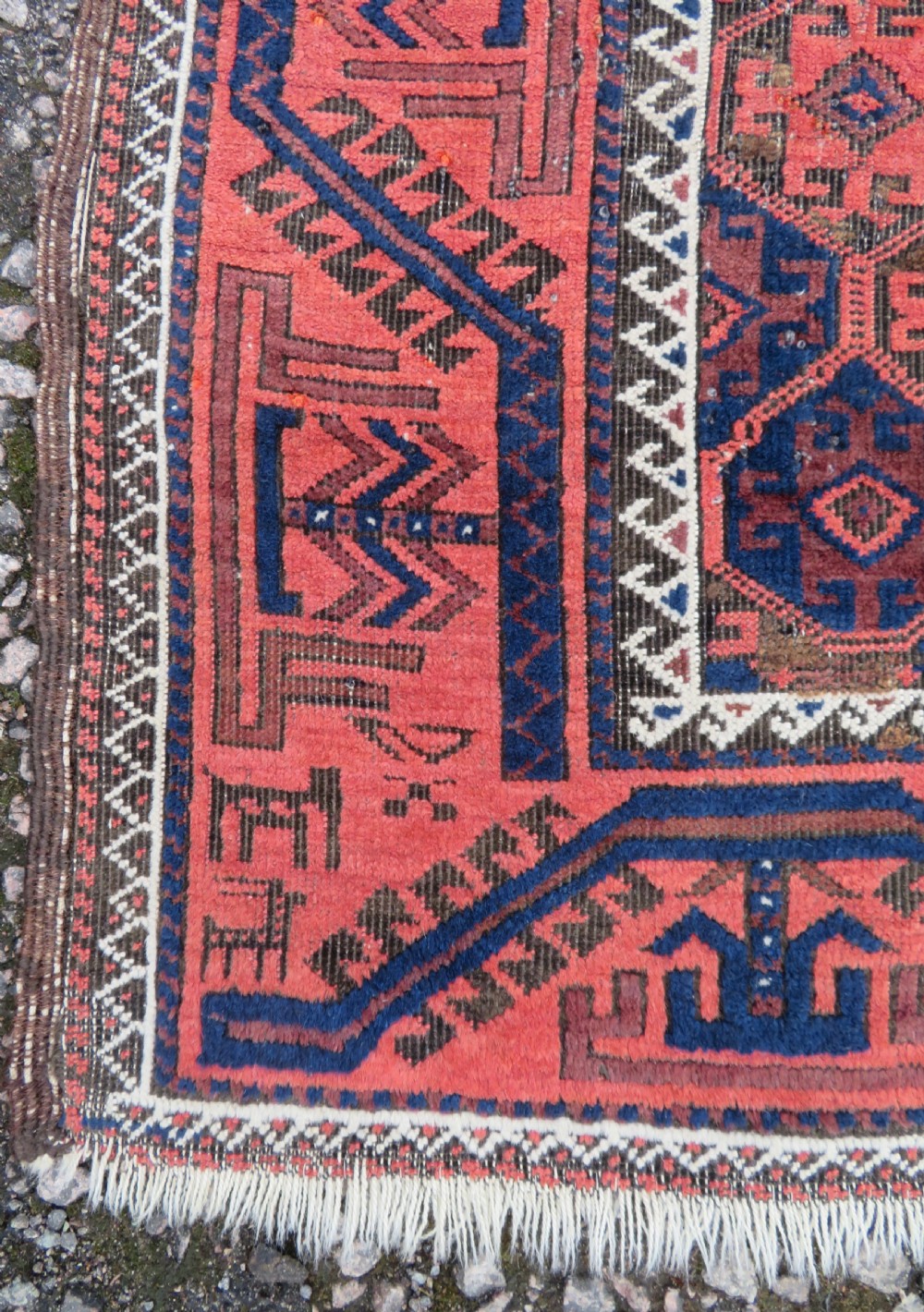 An antique hand-knotted Baluch wool rug featuring repeating geometric diamond motifs in deep red, navy blue, and brown tones with fringed ends. View VII