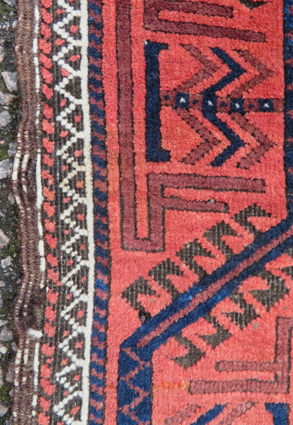 An antique hand-knotted Baluch wool rug featuring repeating geometric diamond motifs in deep red, navy blue, and brown tones with fringed ends. View IX