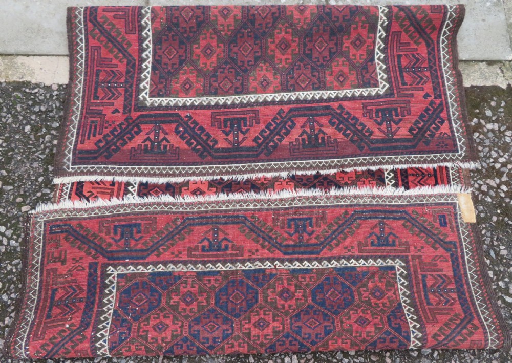 An antique hand-knotted Baluch wool rug featuring repeating geometric diamond motifs in deep red, navy blue, and brown tones with fringed ends. View XIII