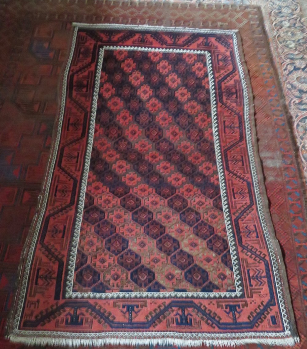 An antique hand-knotted Baluch wool rug featuring repeating geometric diamond motifs in deep red, navy blue, and brown tones with fringed ends. View XVII