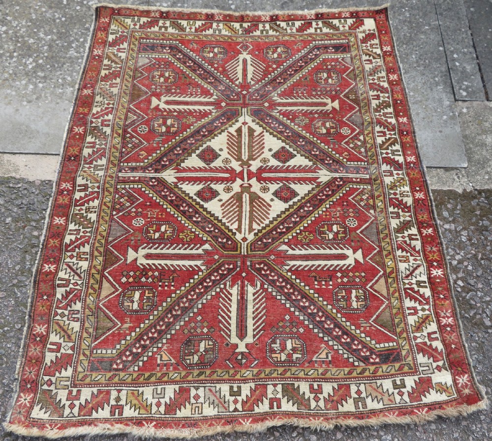 An antique hand-knotted Shirvan wool rug featuring a central diamond medallion, geometric motifs, and detailed borders in shades of red, cream, and brown.