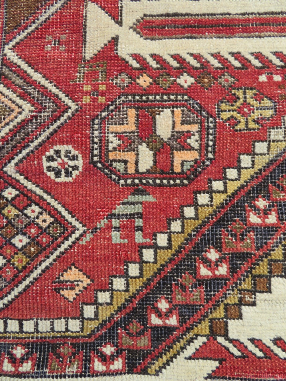 An antique hand-knotted Shirvan wool rug featuring a central diamond medallion, geometric motifs, and detailed borders in shades of red, cream, and brown. View V