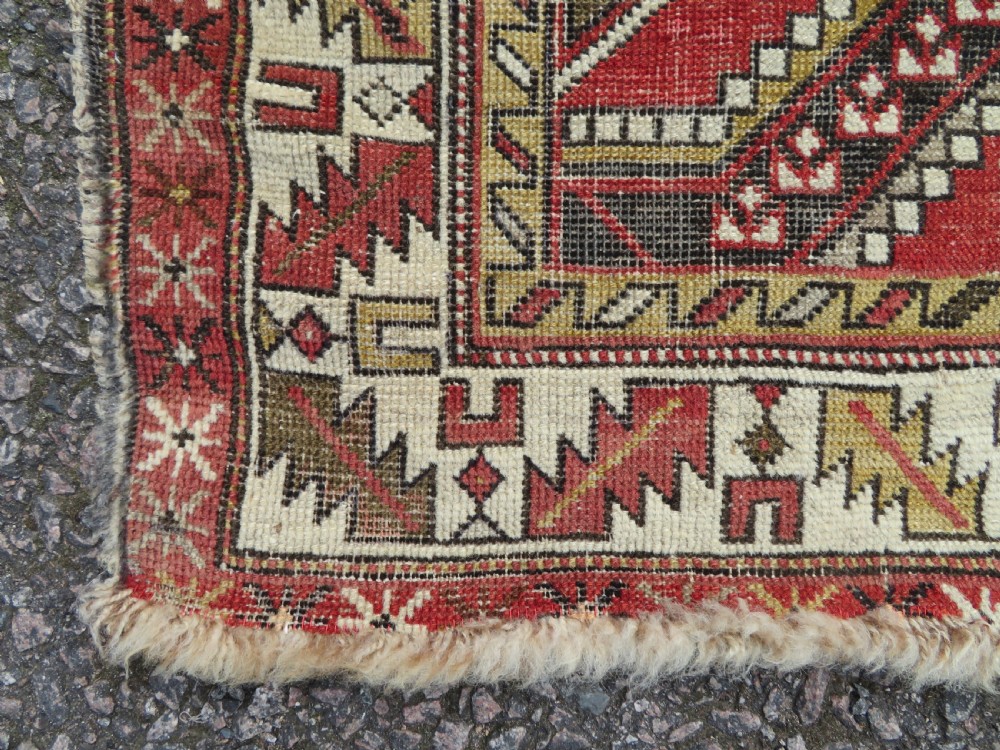 An antique hand-knotted Shirvan wool rug featuring a central diamond medallion, geometric motifs, and detailed borders in shades of red, cream, and brown. View IX