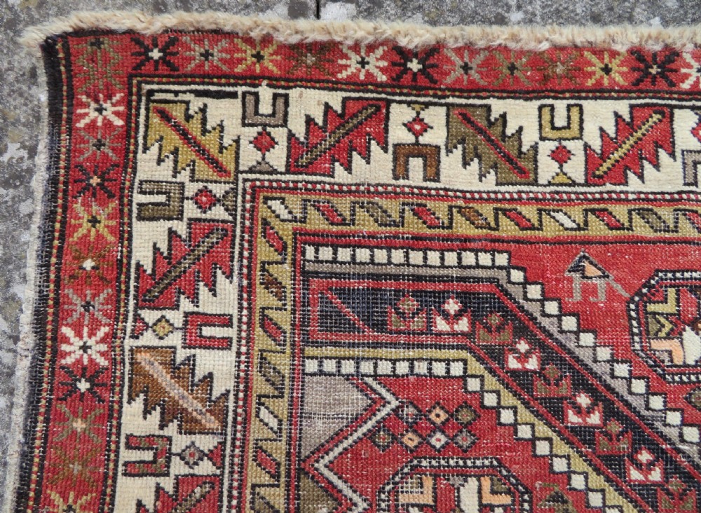 An antique hand-knotted Shirvan wool rug featuring a central diamond medallion, geometric motifs, and detailed borders in shades of red, cream, and brown. View X