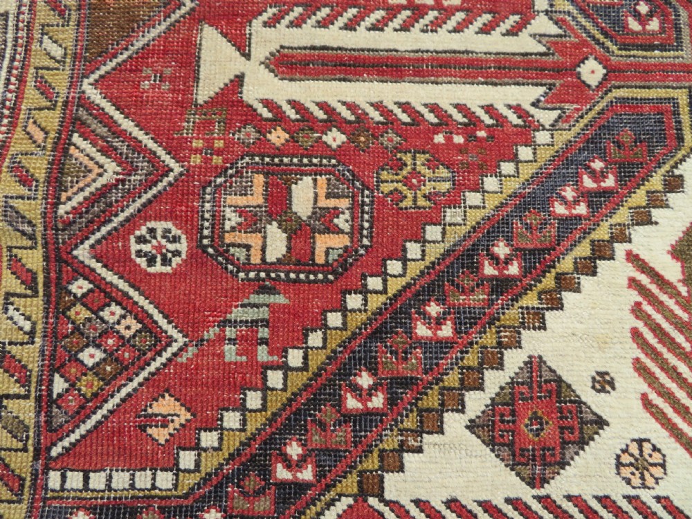 An antique hand-knotted Shirvan wool rug featuring a central diamond medallion, geometric motifs, and detailed borders in shades of red, cream, and brown. View XII