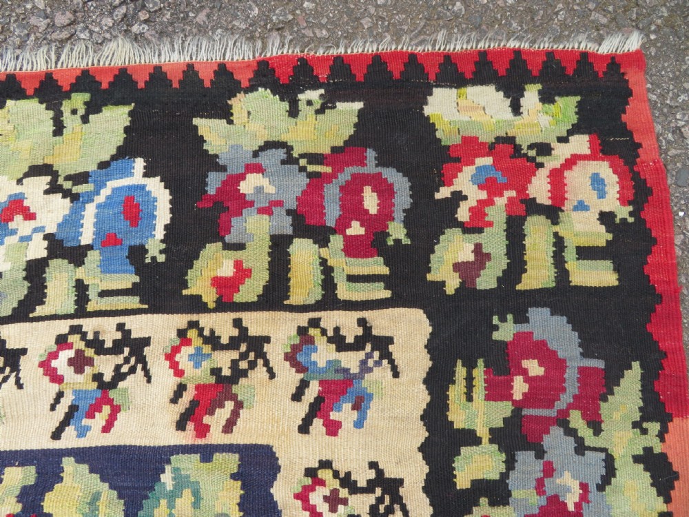 An antique flatweave wool rug featuring a central red panel with blue floral motifs, bordered by dark navy and cream botanical patterns. View VII