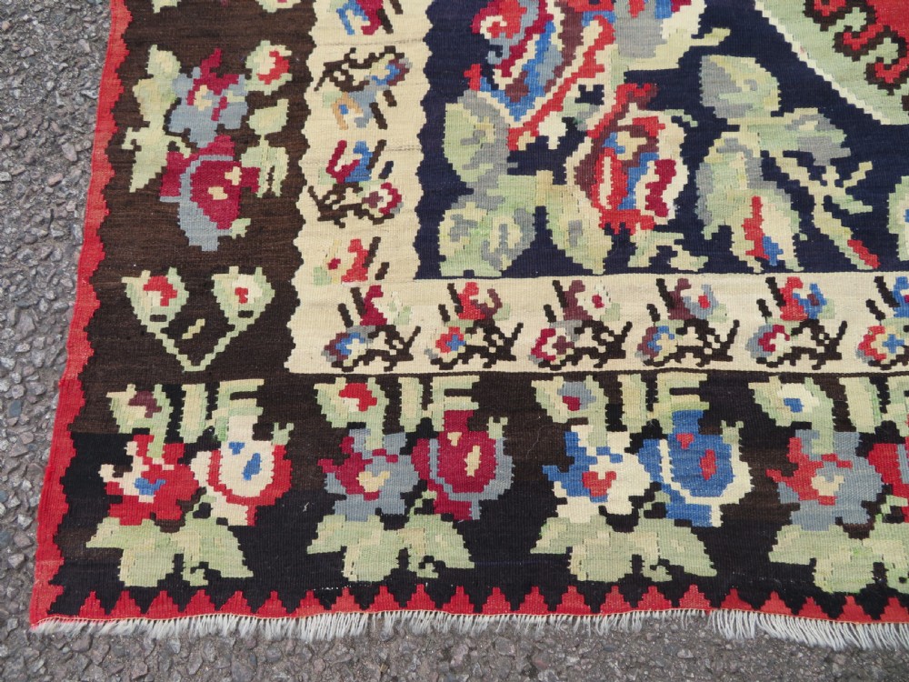 An antique flatweave wool rug featuring a central red panel with blue floral motifs, bordered by dark navy and cream botanical patterns. View VIII