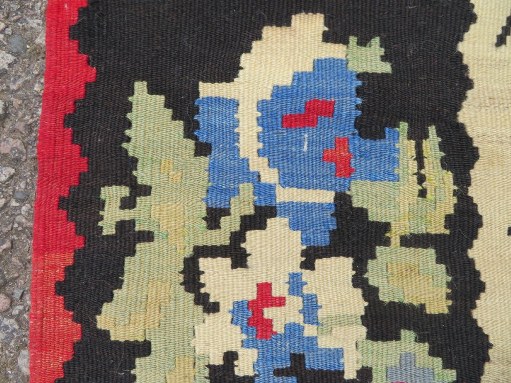 An antique flatweave wool rug featuring a central red panel with blue floral motifs, bordered by dark navy and cream botanical patterns. View XIV