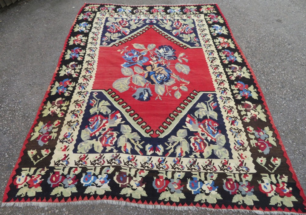 An antique flatweave wool rug featuring a central red panel with blue floral motifs, bordered by dark navy and cream botanical patterns. View XVIII
