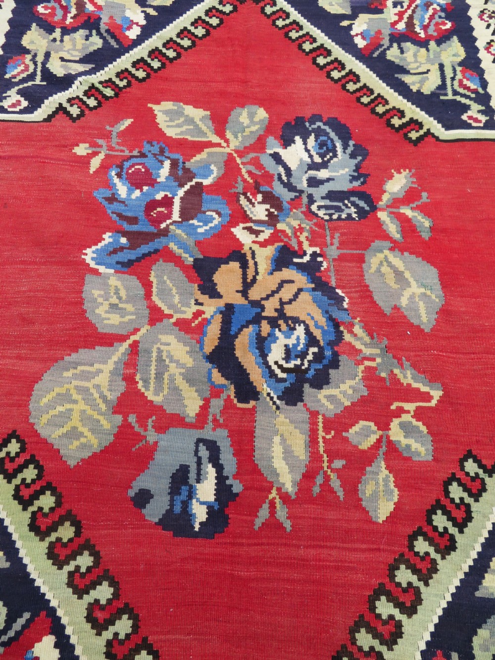 An antique flatweave wool rug featuring a central red panel with blue floral motifs, bordered by dark navy and cream botanical patterns. View XIX