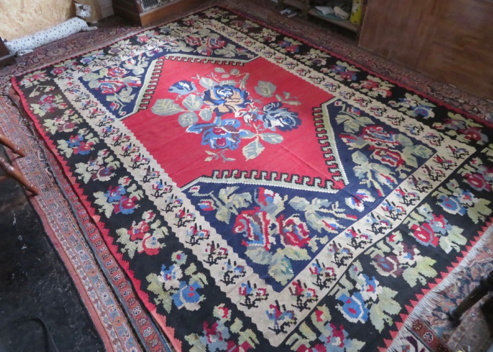 An antique flatweave wool rug featuring a central red panel with blue floral motifs, bordered by dark navy and cream botanical patterns. View XX