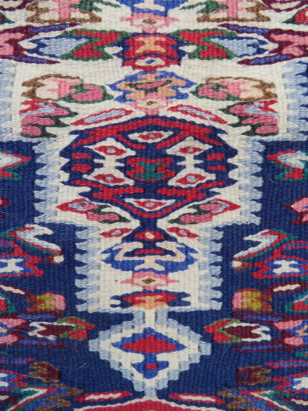 A long, narrow hand-woven Persian Senneh kilim runner featuring a stepped geometric diamond pattern in cream and navy blue bordered by a red outer frame with fringed ends. View II