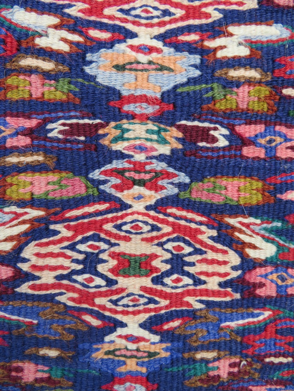 A long, narrow hand-woven Persian Senneh kilim runner featuring a stepped geometric diamond pattern in cream and navy blue bordered by a red outer frame with fringed ends. View III