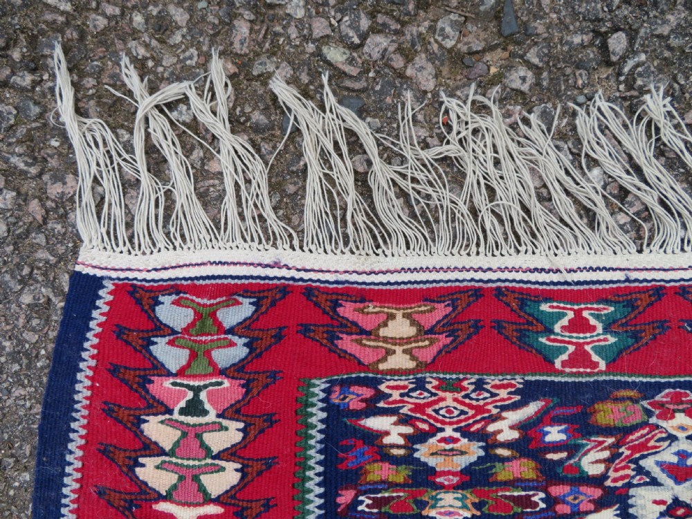 A long, narrow hand-woven Persian Senneh kilim runner featuring a stepped geometric diamond pattern in cream and navy blue bordered by a red outer frame with fringed ends. View VIII
