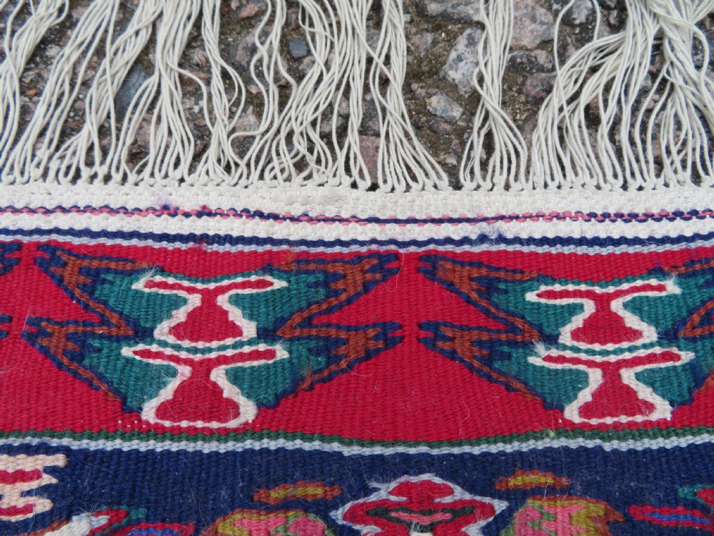 A long, narrow hand-woven Persian Senneh kilim runner featuring a stepped geometric diamond pattern in cream and navy blue bordered by a red outer frame with fringed ends. View XIV