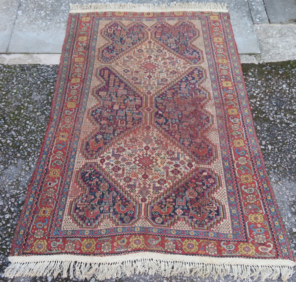 An antique Khamseh nomadic wool rug featuring complex geometric medallions, bird motifs, and multi-layered borders in terracotta, navy blue, and cream.