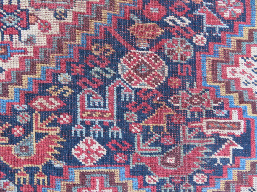 An antique Khamseh nomadic wool rug featuring complex geometric medallions, bird motifs, and multi-layered borders in terracotta, navy blue, and cream. View X