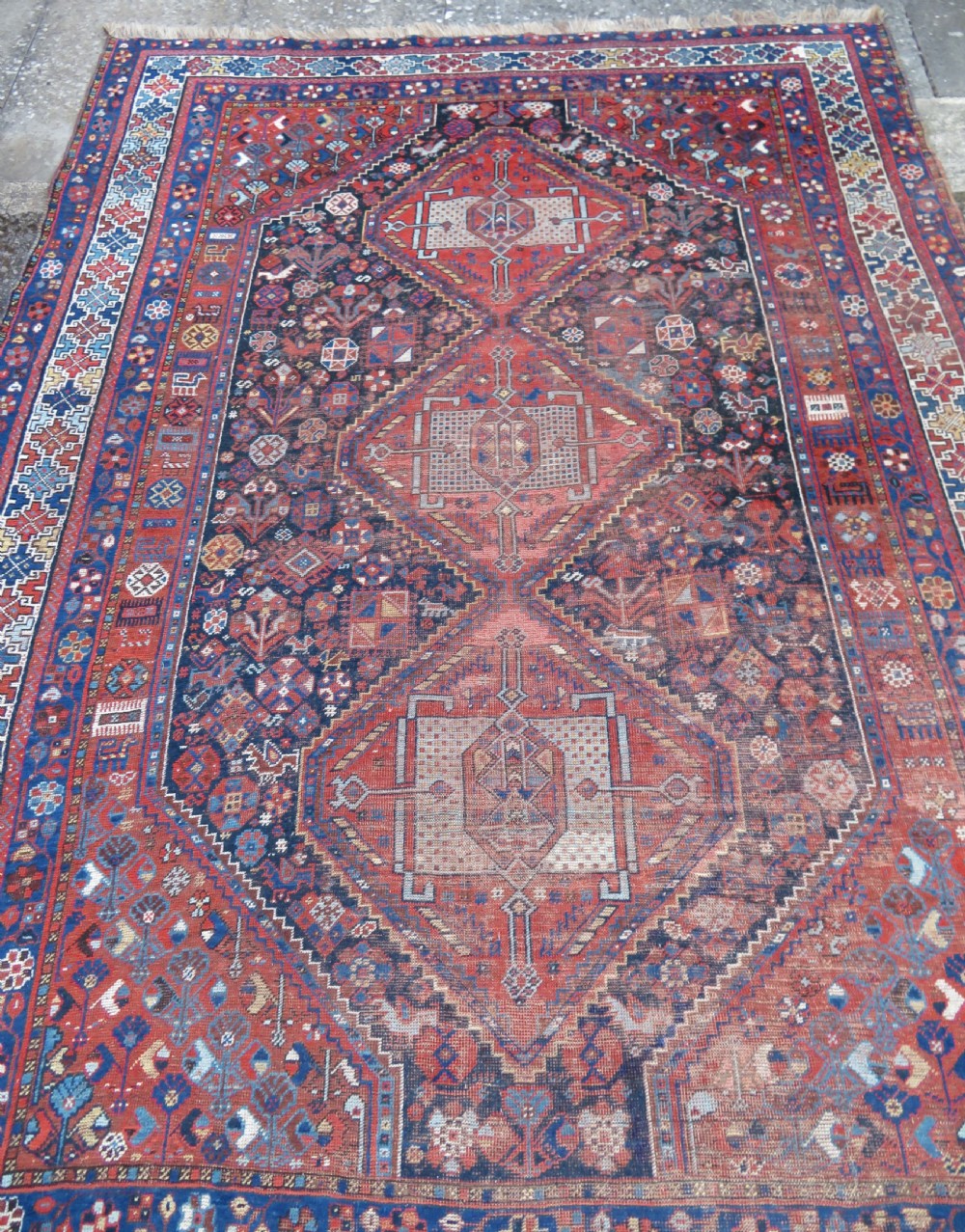 An antique Persian Khamseh wool carpet featuring a dark navy blue field with three stacked diamond medallions and geometric borders in terracotta red and ivory. View III