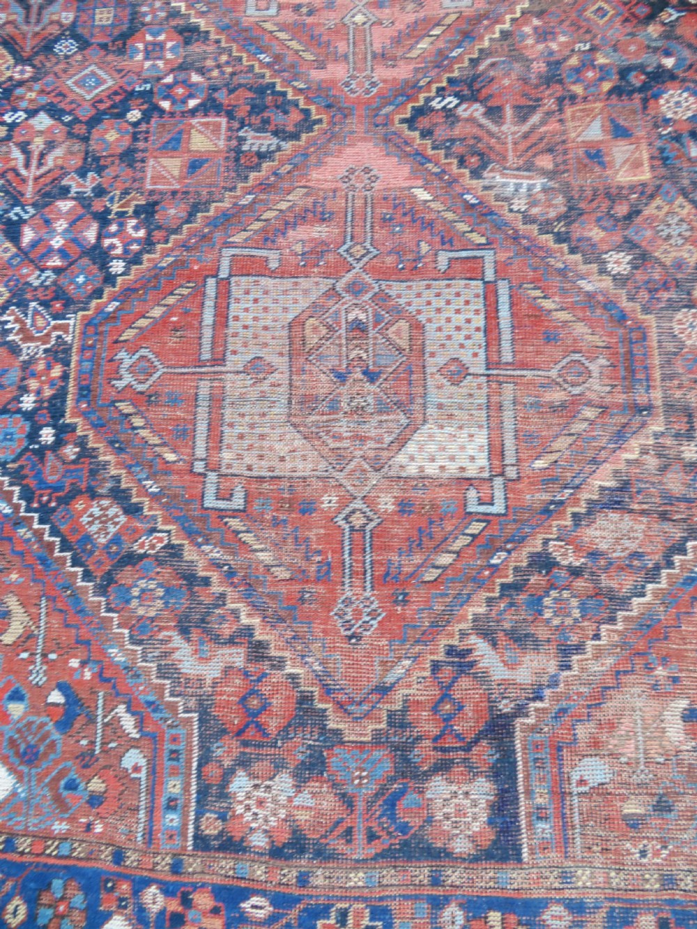 An antique Persian Khamseh wool carpet featuring a dark navy blue field with three stacked diamond medallions and geometric borders in terracotta red and ivory. View VIII