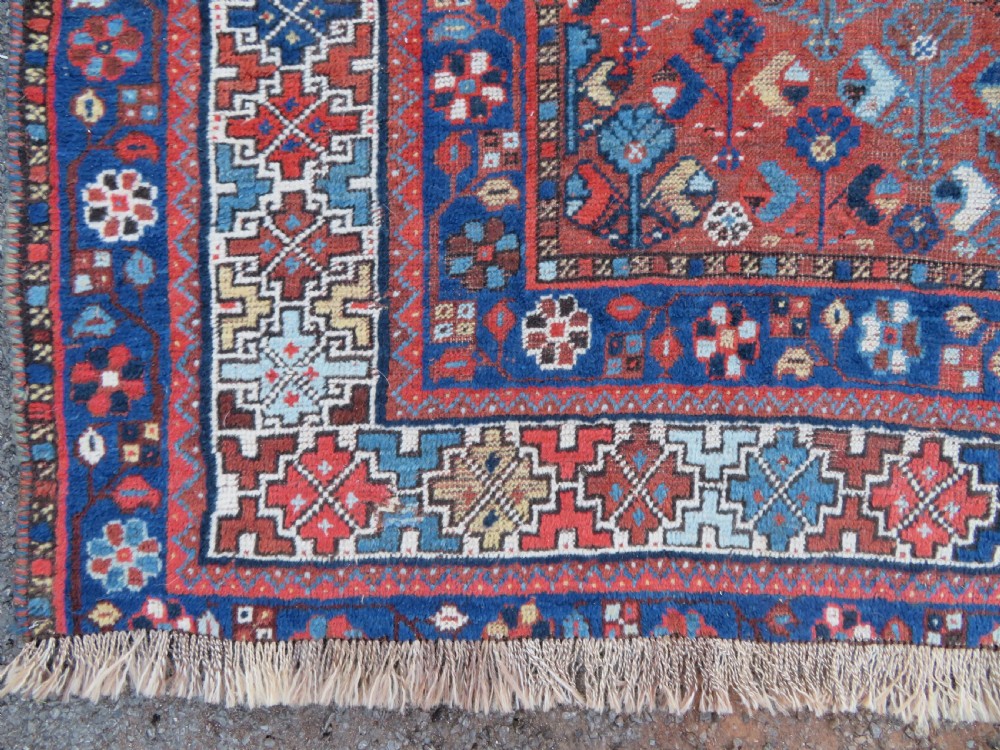 An antique Persian Khamseh wool carpet featuring a dark navy blue field with three stacked diamond medallions and geometric borders in terracotta red and ivory. View IX
