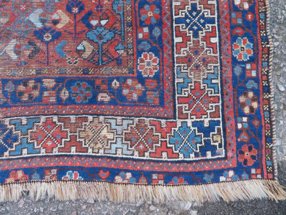 An antique Persian Khamseh wool carpet featuring a dark navy blue field with three stacked diamond medallions and geometric borders in terracotta red and ivory. View X